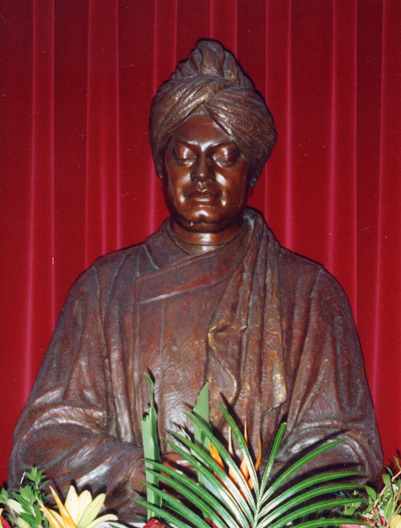 Metal sculpture of Swami Vivekananda seated surrounded by flowers.