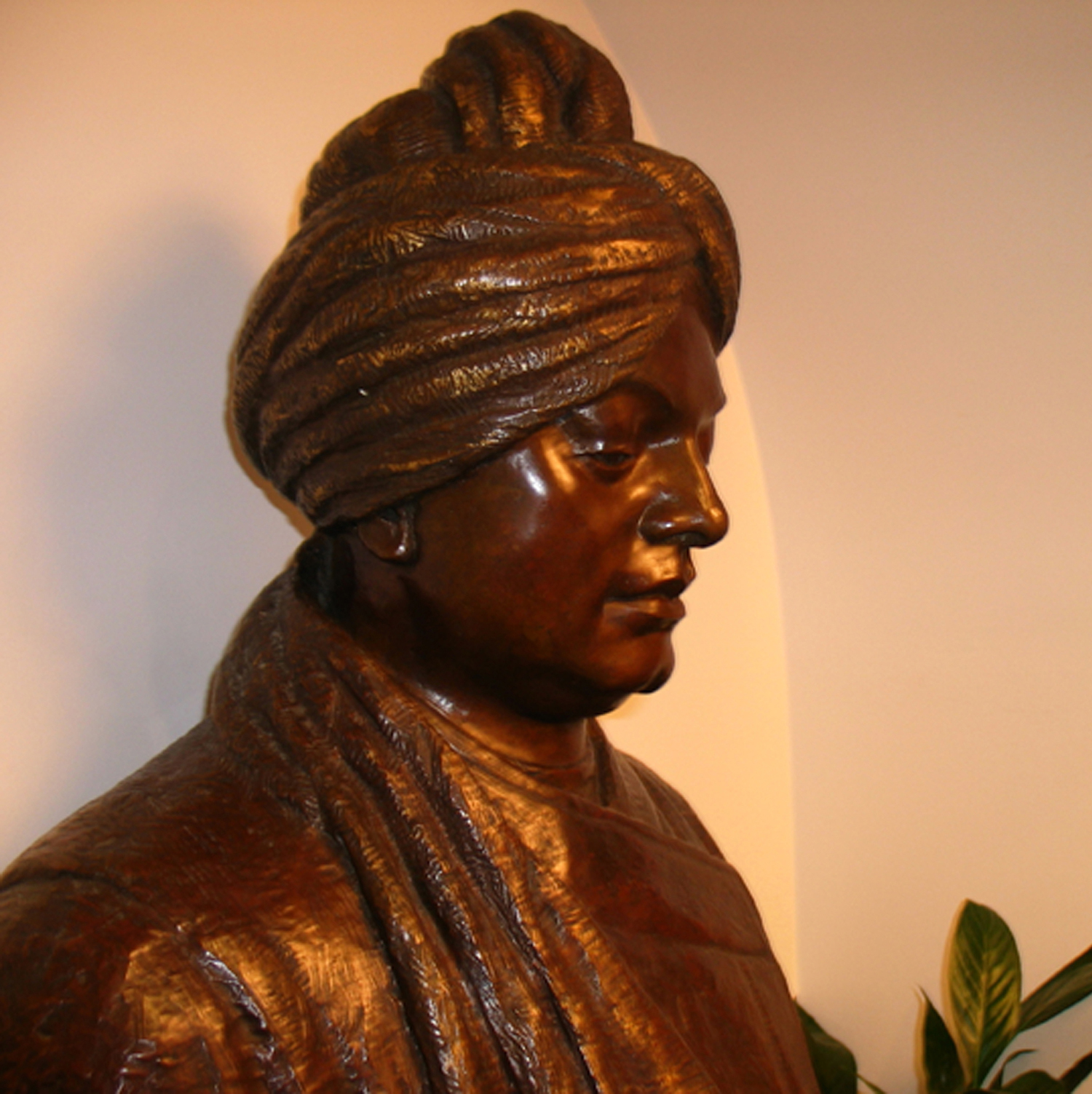 Metal sculpture of Swami Vivekananda seated surrounded by flowers.